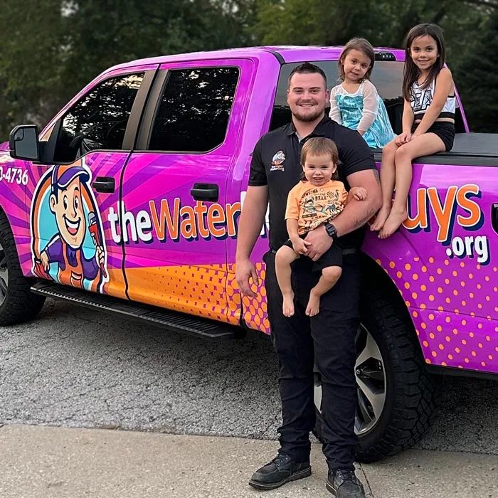 Dean Cribaro holding his son with his two daughters seated on the bed of the Water Heater Guys truck