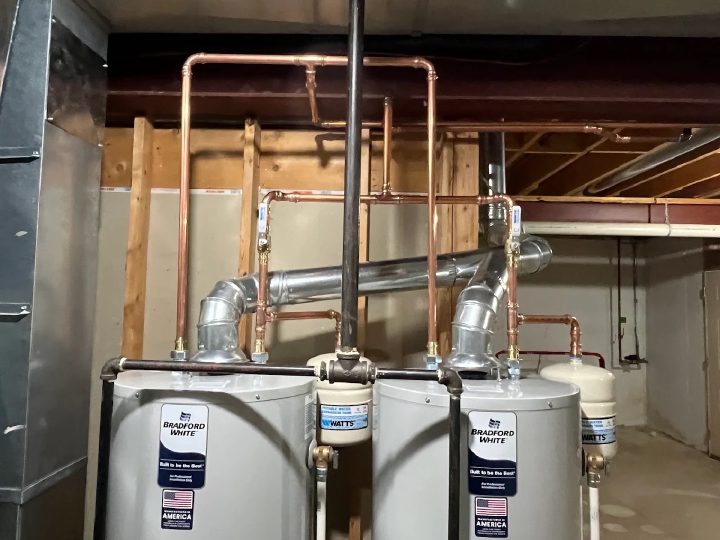 Two Bradford White tank water heaters installed side by side in a Kane County basement, with copper supply lines and code-compliant metal flue venting